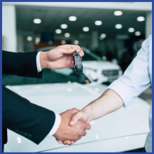 Two people hand shake over the keys to a car.